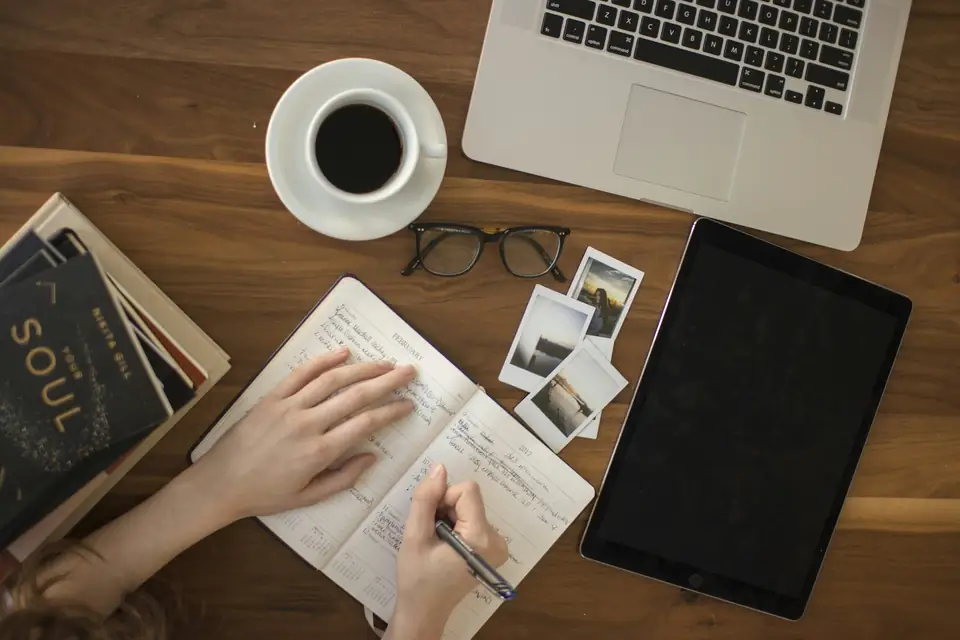 Hands writing notes at a desk with a laptop and coffee