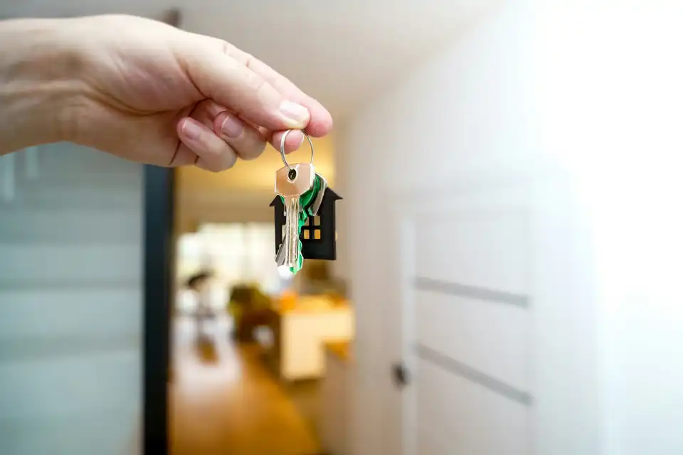 Hand holding house keys in a bright hallway