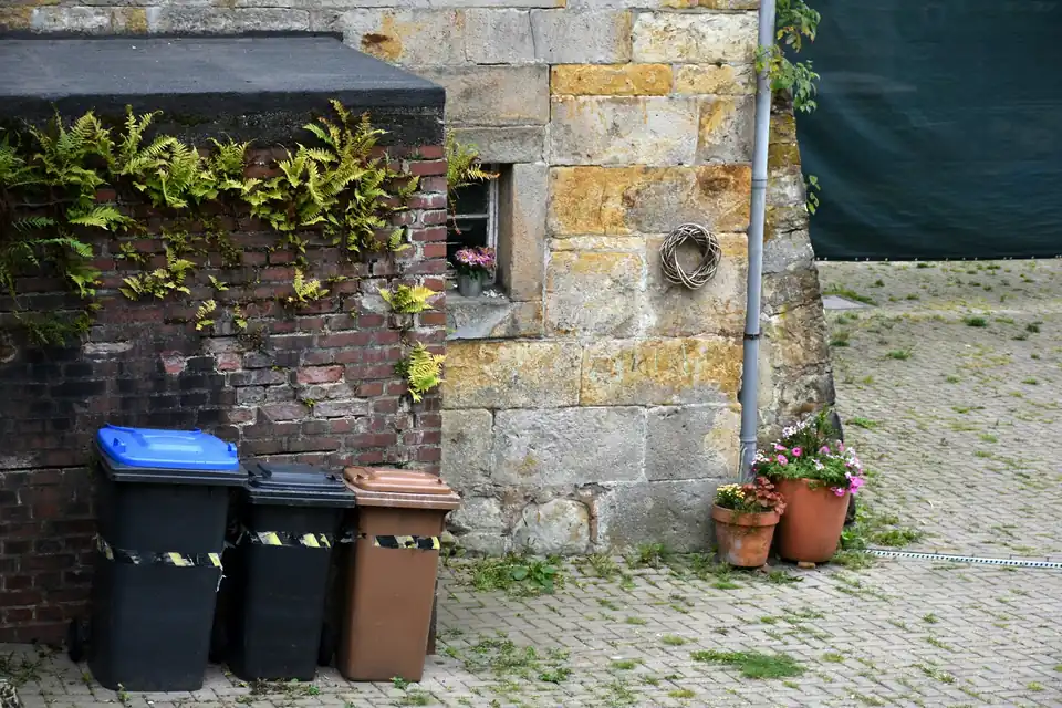 Waste bins with coloured lids next to a stone building